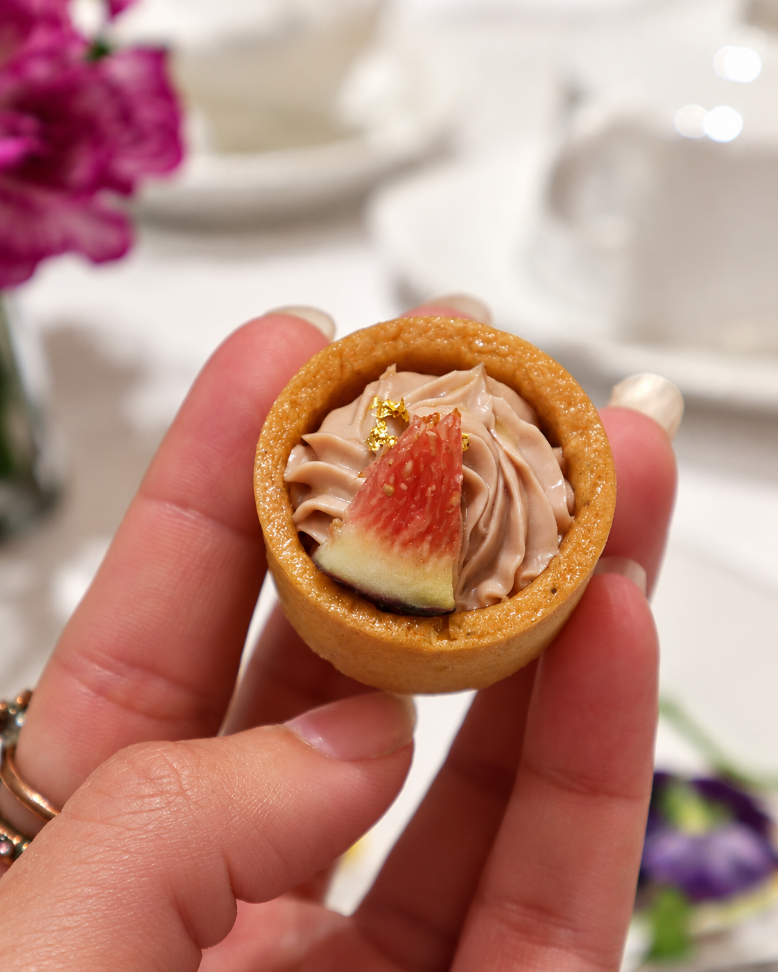 Close-up of a miniature fruit tart held by hand at Caf&eacute; Parlour, 1881 Heritage Hong Kong, featuring a golden pastry shell, cream filling, fresh fig slices, and delicate decorative toppings.