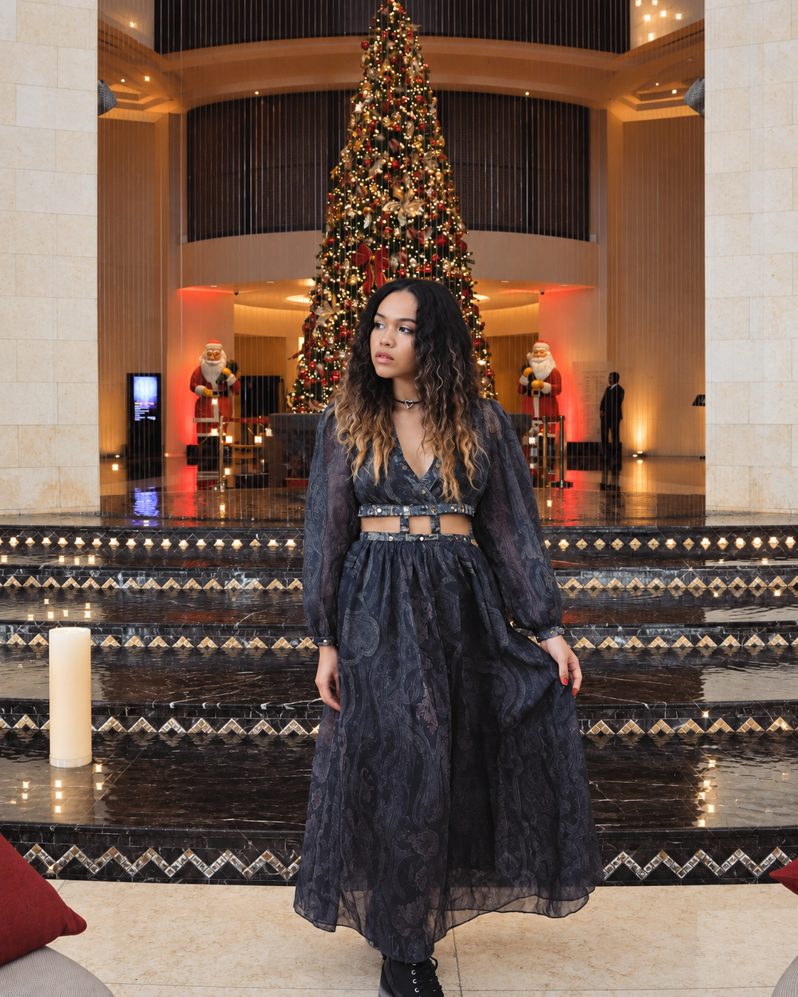 Rosi Ross wearing a flowing dark Zimmermann designer outfit with intricate detailing, posing on an ornate staircase inside Raffles Dubai during the festive Christmas season.