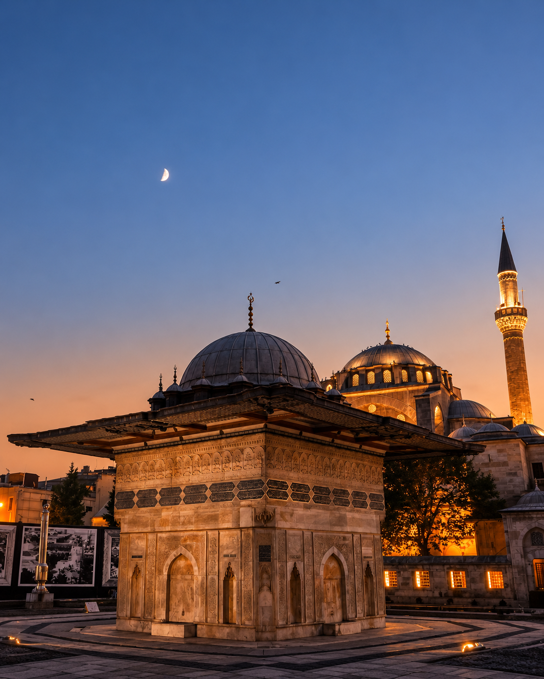 Historic Ottoman mosque in Istanbul at twilight, featuring illuminated domes, a tall minaret, ornate stone architecture, and a warm orange-pink sunset sky.