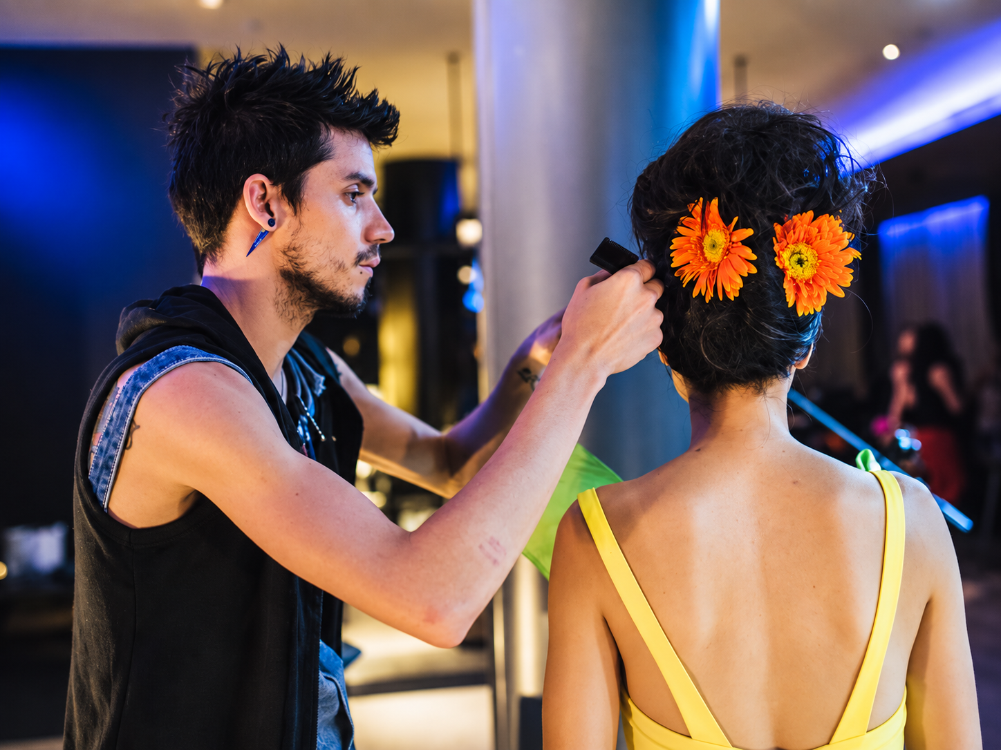Model receiving hairstyling with floral accessories during backstage beauty preparation for fashion night.
