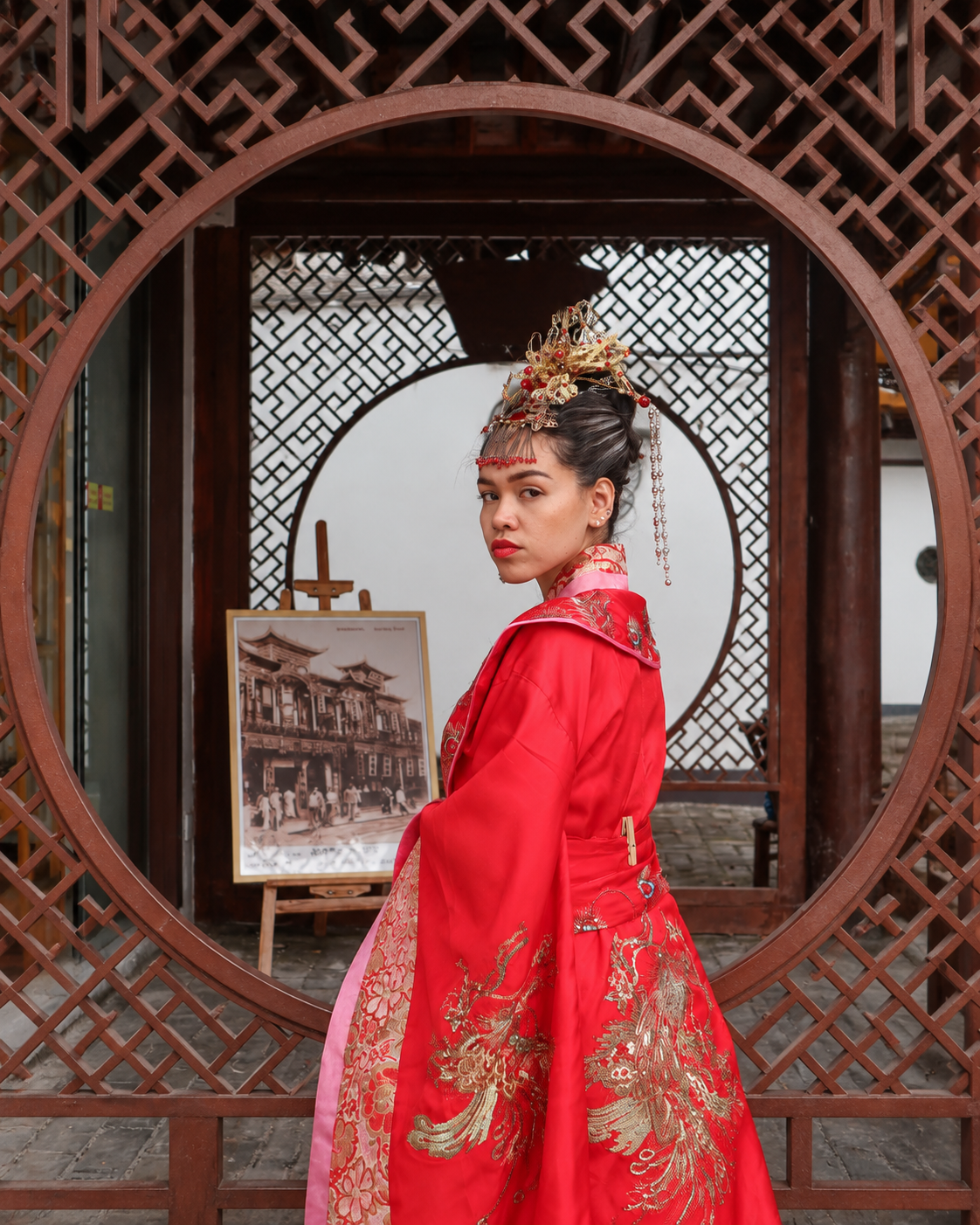 Rosi Ross wearing red Chinese Hanfu framed by a traditional moon gate in a Chinese garden.