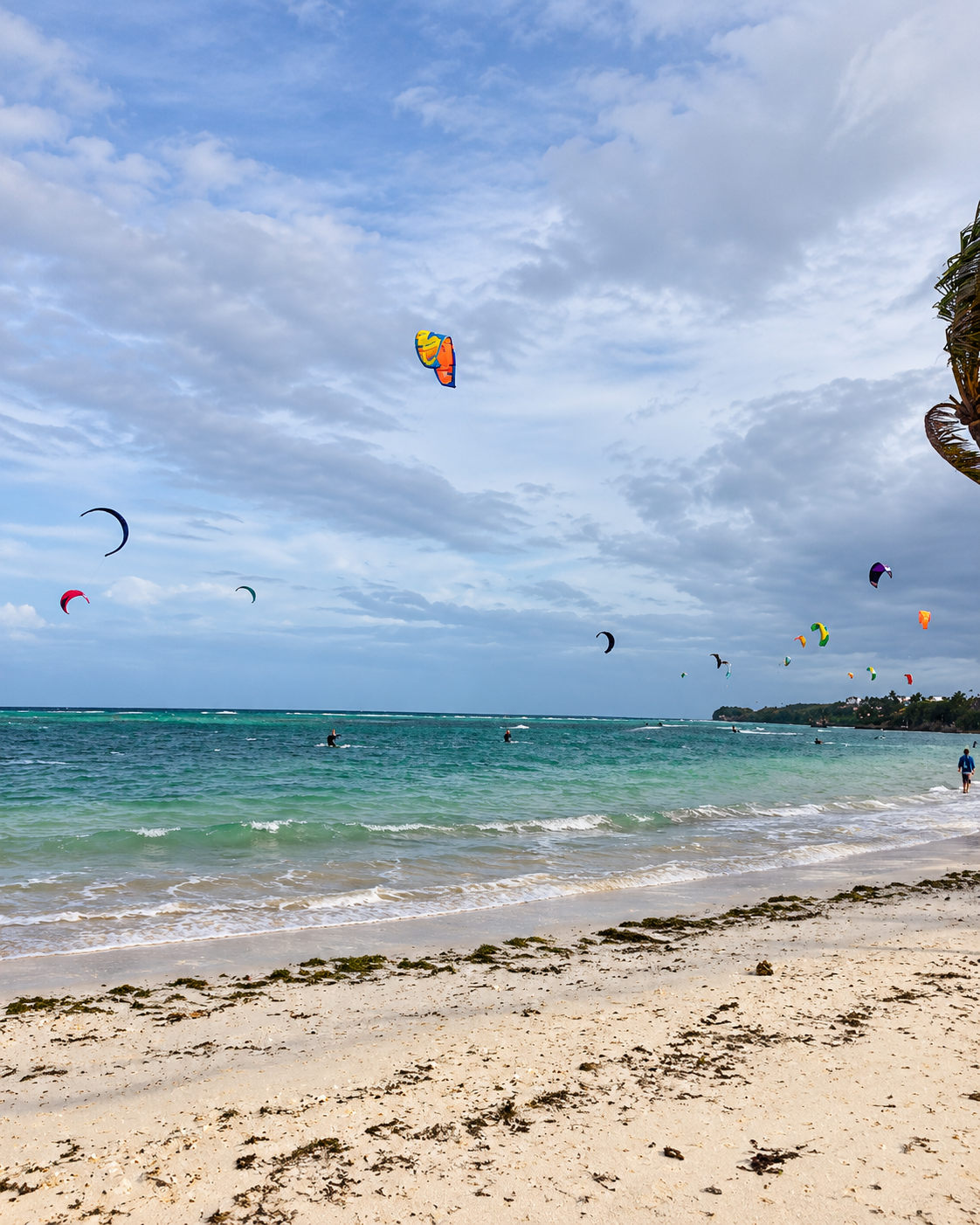 Puka Shell Beach in Boracay, Philippines, with turquoise water, tropical shoreline, and kitesurfers in the distance.