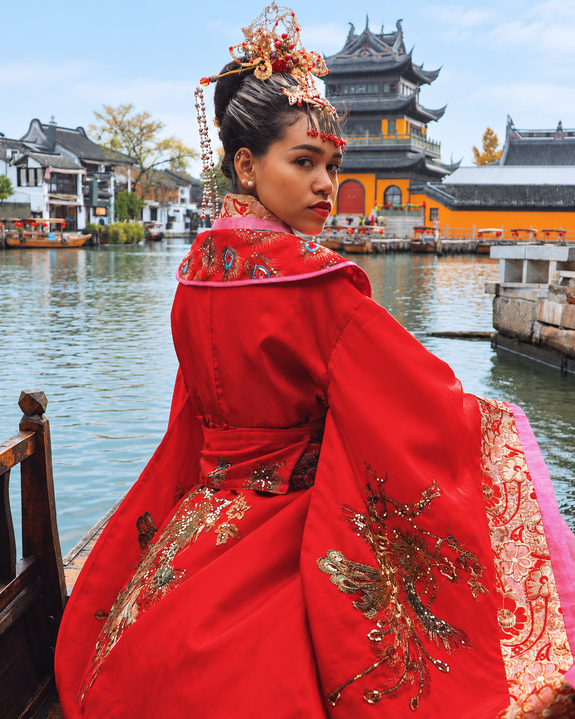 Rosi Ross modeling an ornate red Hanfu with embroidered details in a traditional Chinese garden setting.