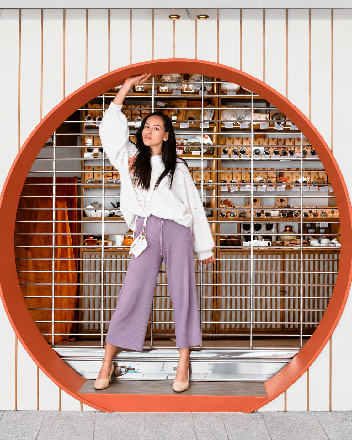 Rosi Ross wearing vintage-inspired fashion with lavender trousers and a white blouse during a photoshoot at a modern museum.
