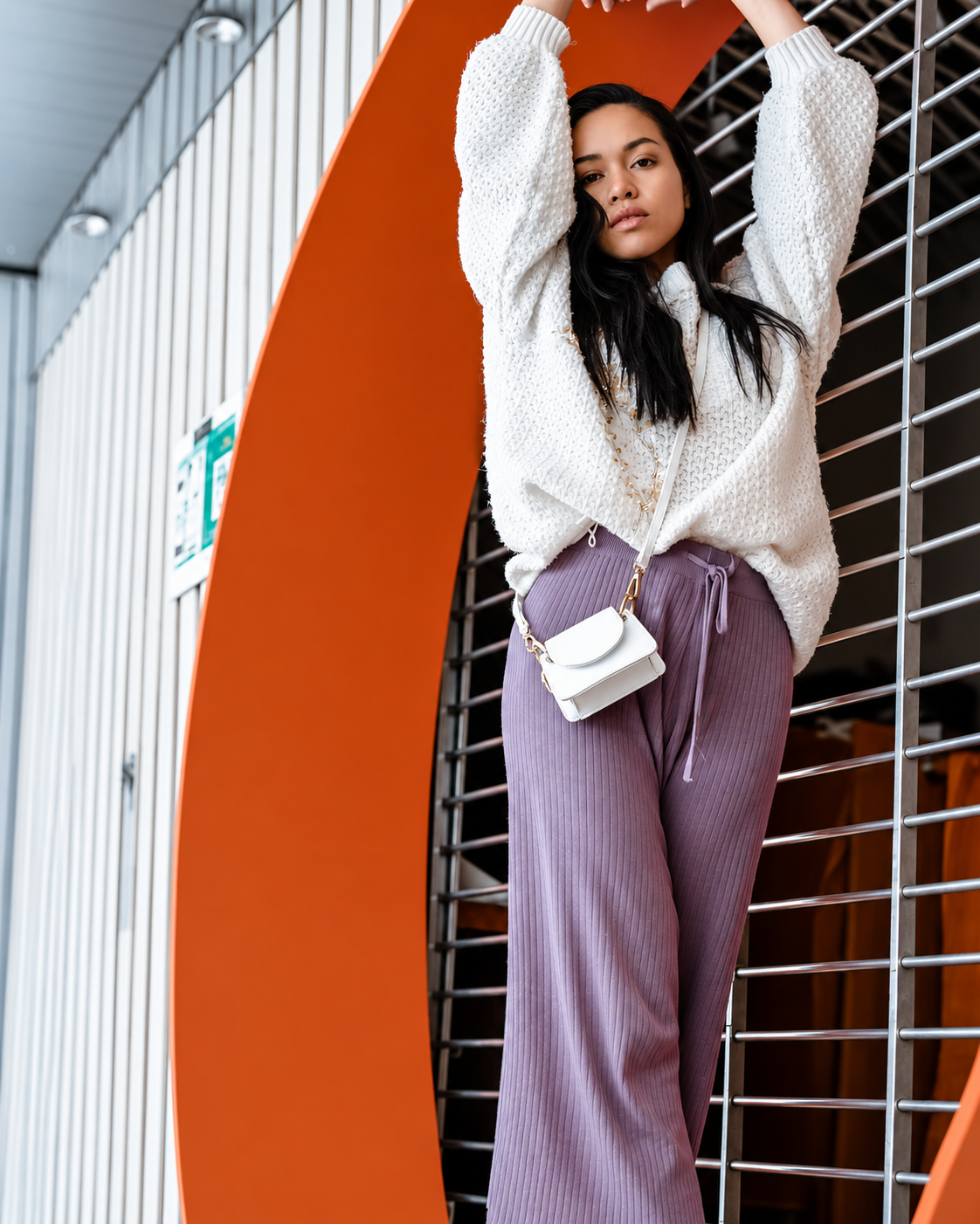Rosi Ross modeling a white blouse, lavender trousers, and vintage accessories at a modern museum, showcasing secondhand fashion styling.