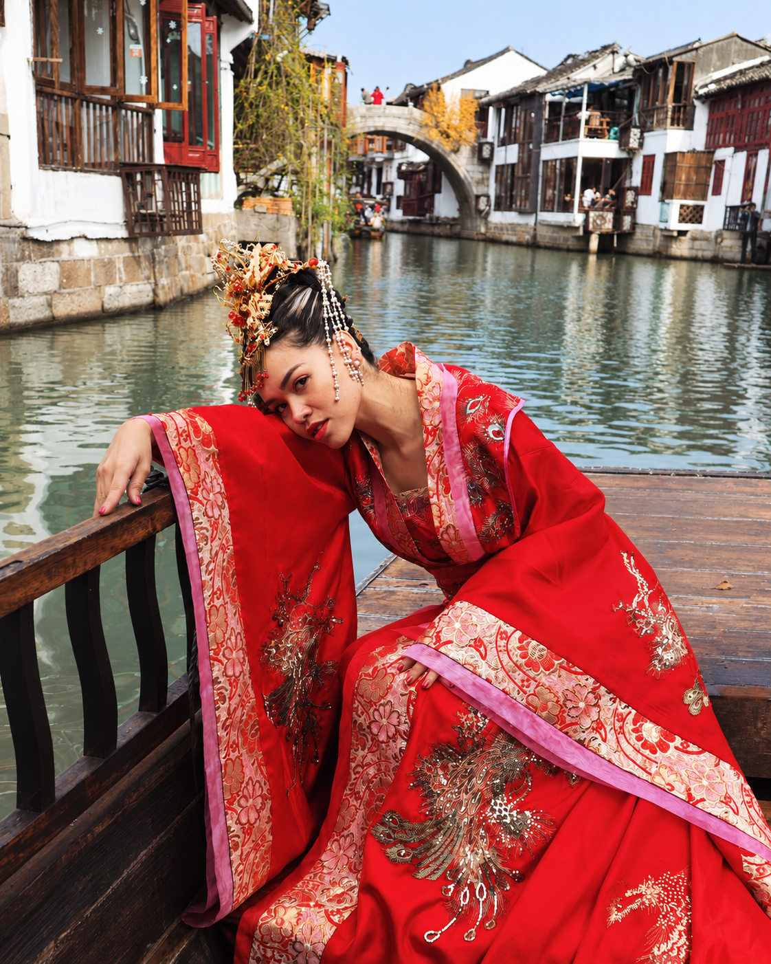Rosi Ross wearing traditional red Chinese Hanfu while posing beside the water in a historic-style Chinese garden.
