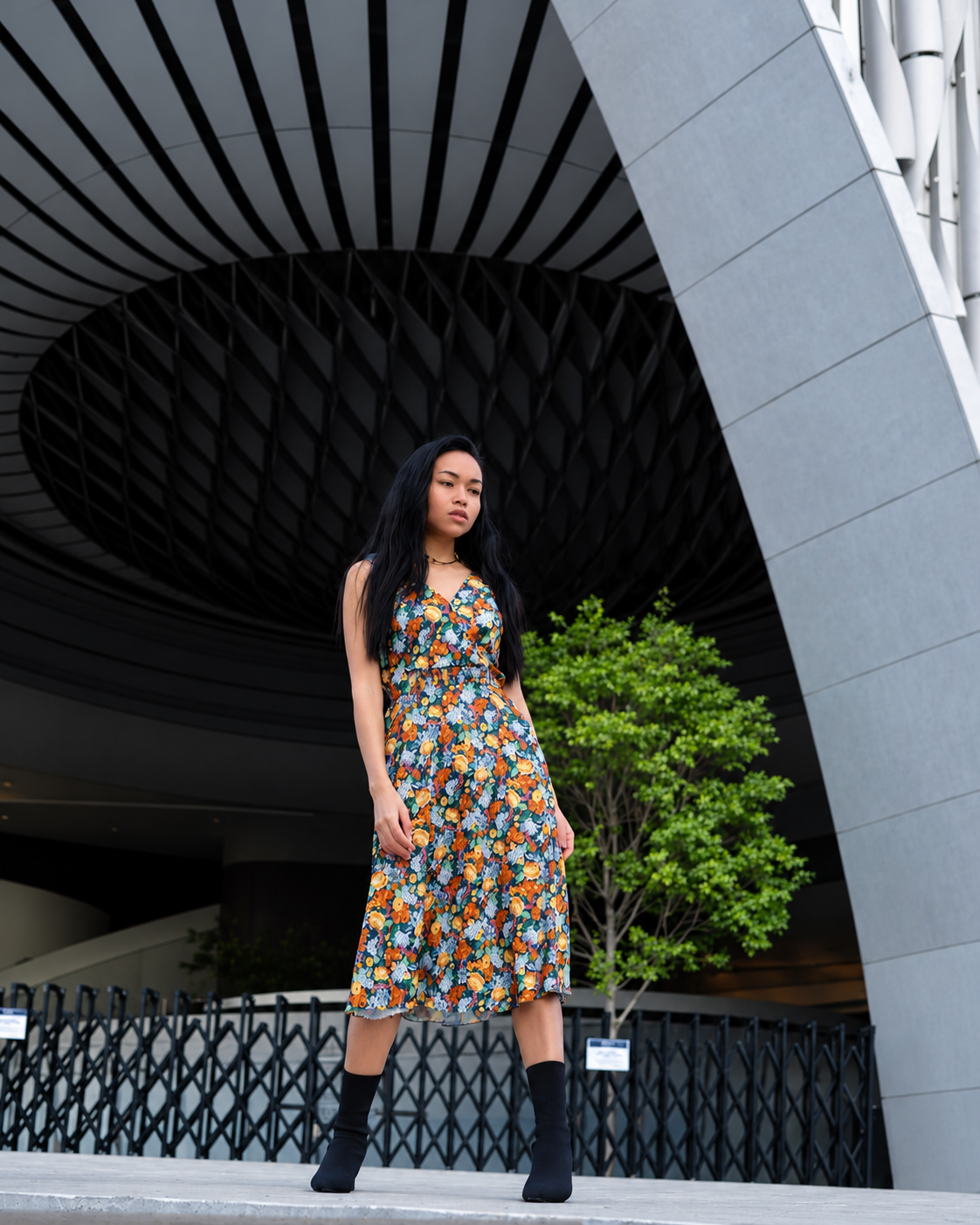Rosi Ross wearing a colorful floral vintage dress and black boots outside a modern museum during a sustainable fashion photoshoot.