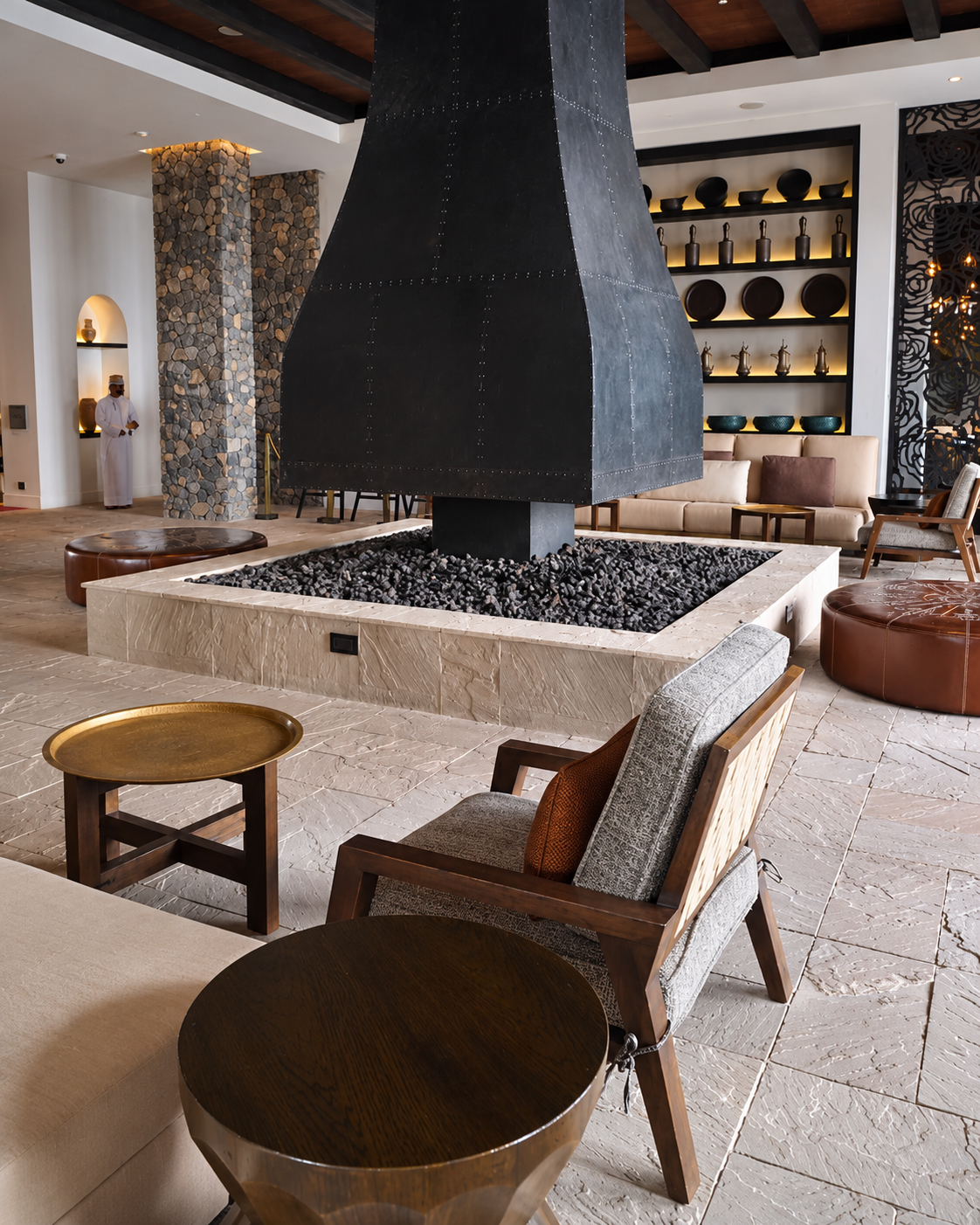 Alila Jabal Akhdar Luxury Lobby Fireplace Lounge Alila Jabal Akhdar hotel lobby featuring a monumental suspended black metal fireplace, natural stone flooring, wooden furniture and contemporary lounge seating.