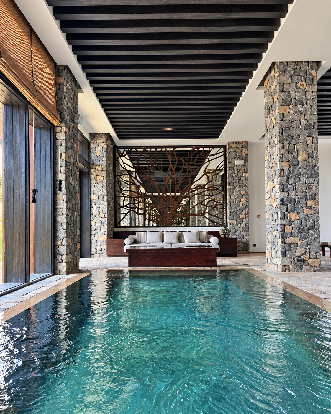 Alila Jabal Akhdar Luxury Pool Lounge with Tree Screen Indoor pool at Alila Jabal Akhdar, Oman, featuring turquoise water, natural stone columns, dark wooden ceiling beams and mountain-inspired architecture.