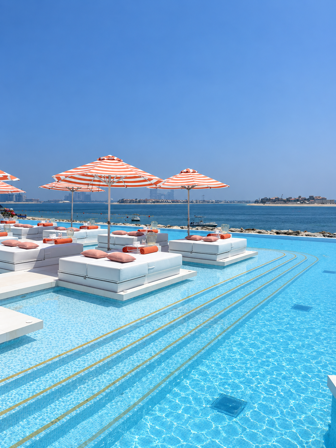 BCH CLB Beach City View Infinity pool, white sunbeds, and striped umbrellas at BCH:CLB Dubai overlooking the Arabian Gulf.