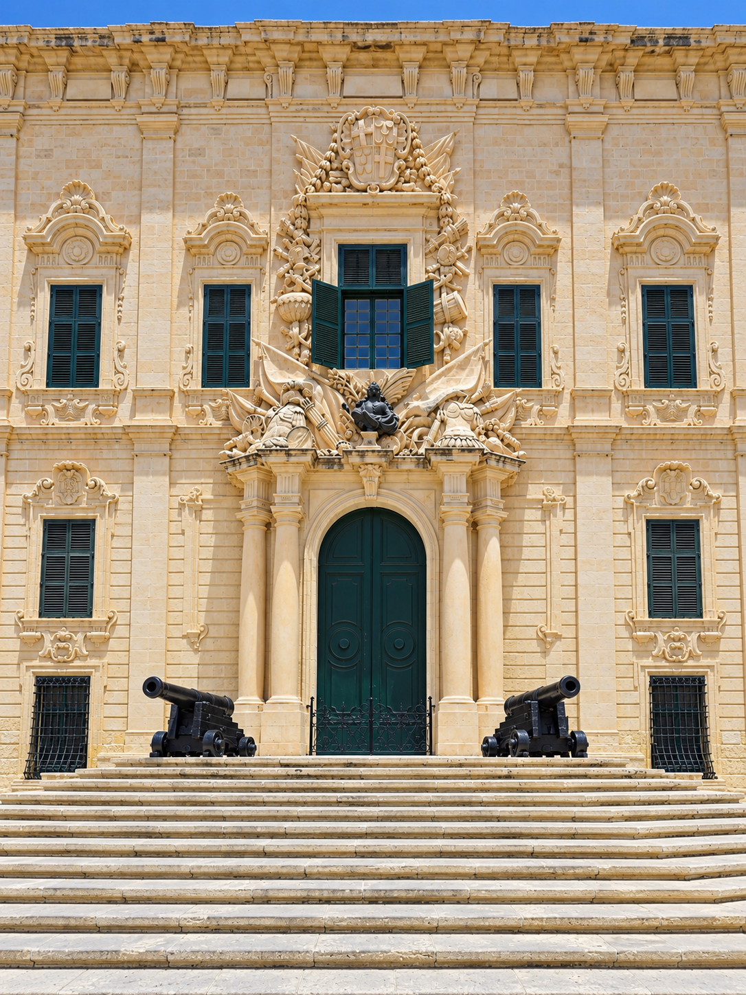 Historic Baroque limestone building with ornate fa&ccedil;ade, green doors, and cannons in Valletta, Malta.