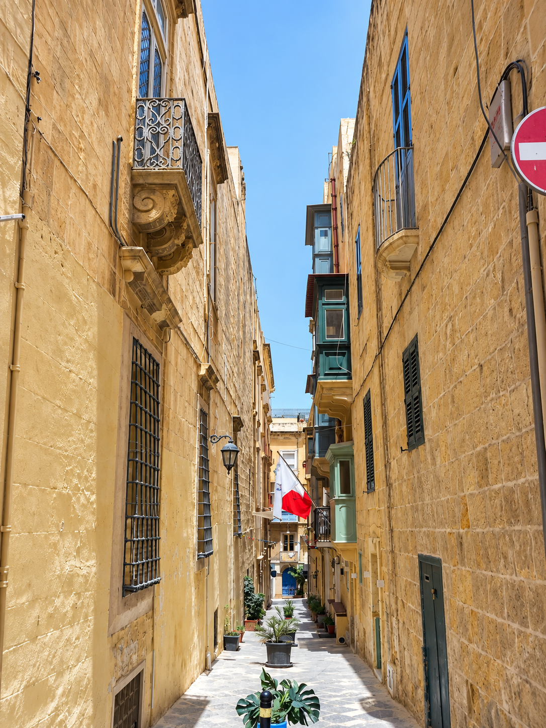Narrow limestone street in Valletta, Malta, featuring traditional colorful Maltese balconies and historic buildings.