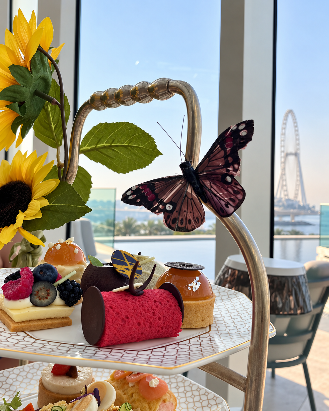 Three-tiered afternoon tea stand with assorted pastries, butterfly decor, and sunflowers at The Address Marina