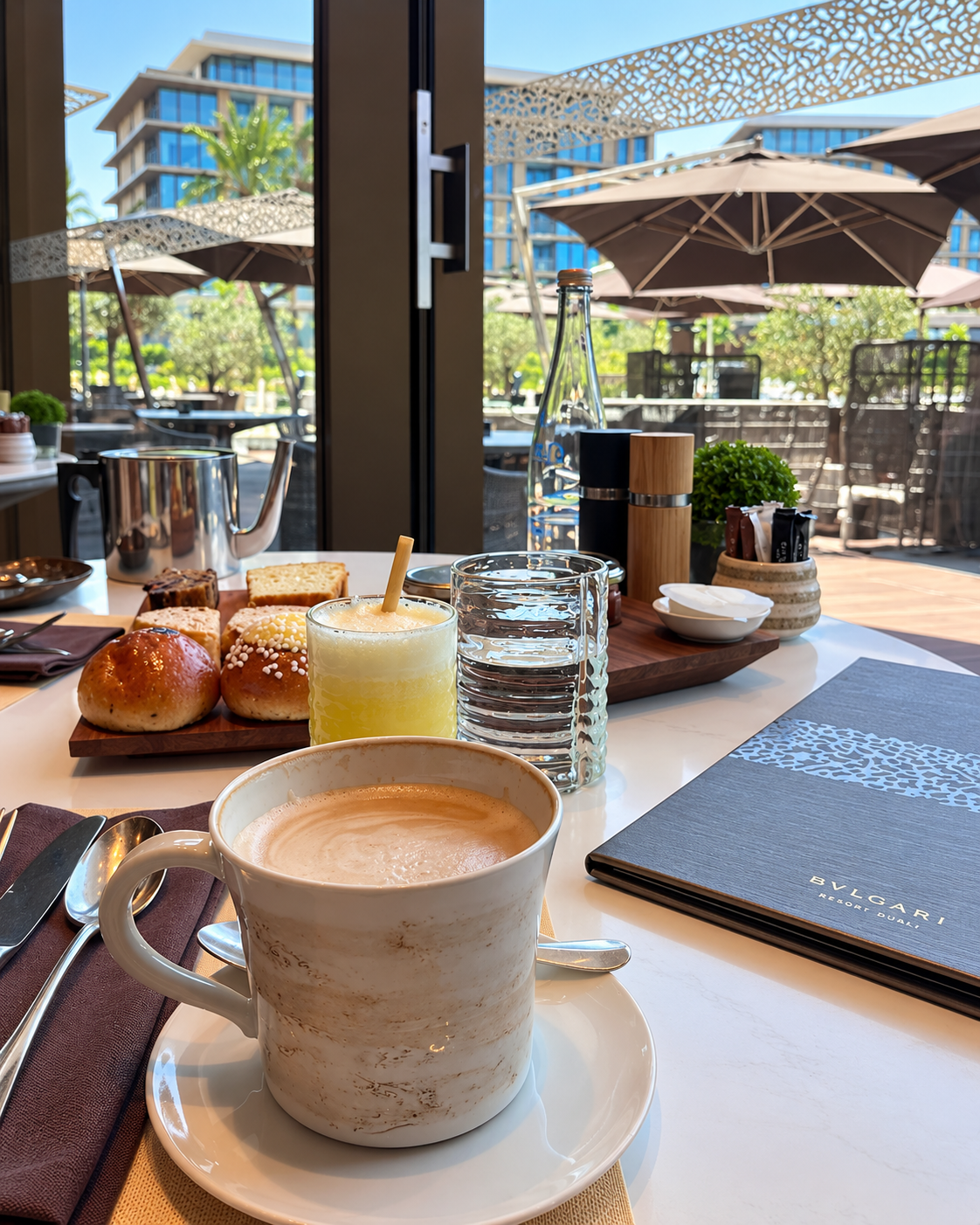 Bvlgari Resort Dubai Aesthetics Breakfast table at Bulgari Resort Dubai featuring coffee, fresh juice, pastries, and elegant table settings.