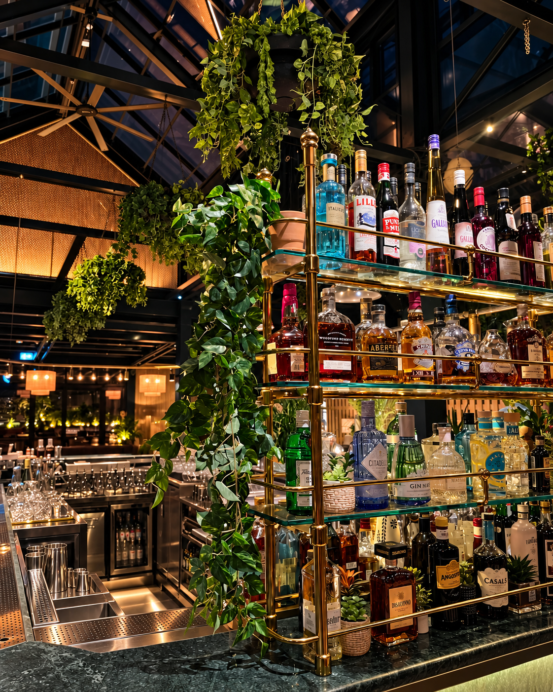 Modern Bar Display at Eugene Eugene An elegant bar with a golden, multi-tiered shelf stocked with various liquor bottles, adorned with lush hanging plants at Eugene Eugene