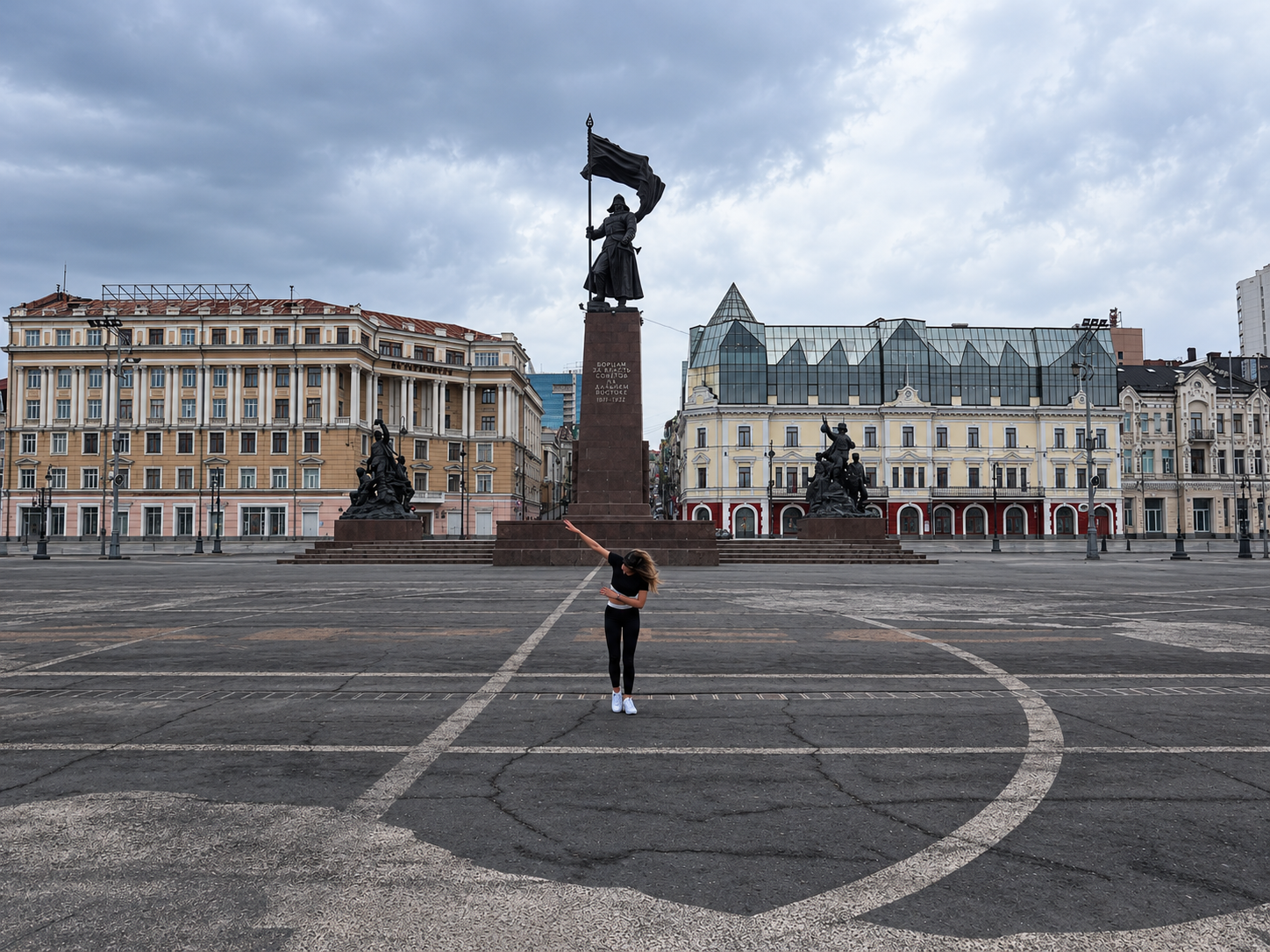 Rosi Ross stands in an open square in Vladivostok, Russia, with large statues and historical buildings in the background.