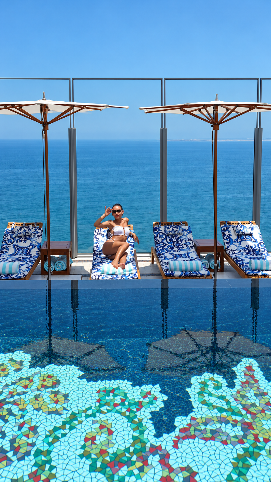 Rosi Ross in white bikini relaxing on a poolside lounge chair with an ocean view. Modern resort design, infinity pool at Cloud22