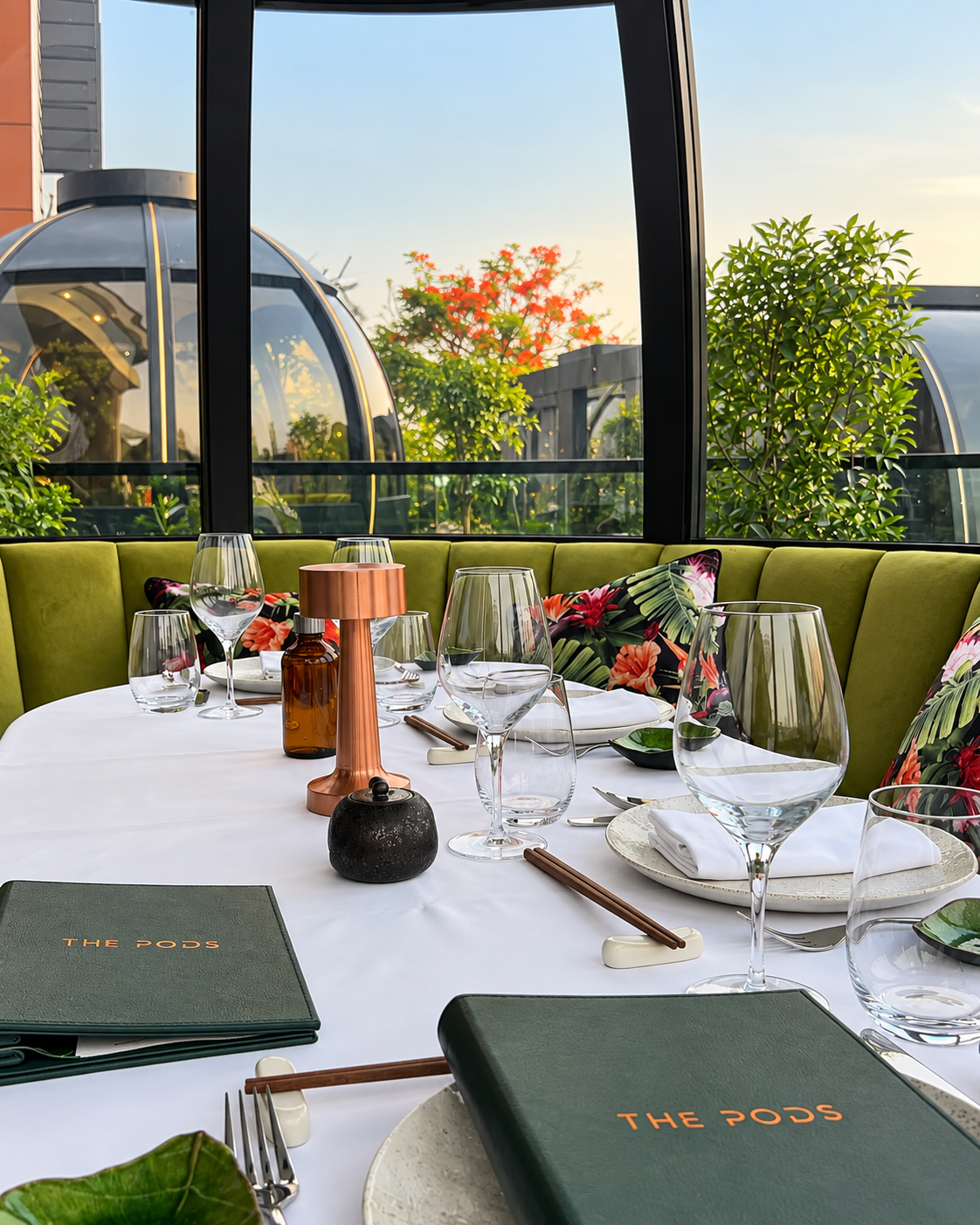 Elegant dining table setup with green seating, glass domes, and foliage view at The Pods Bluewaters.