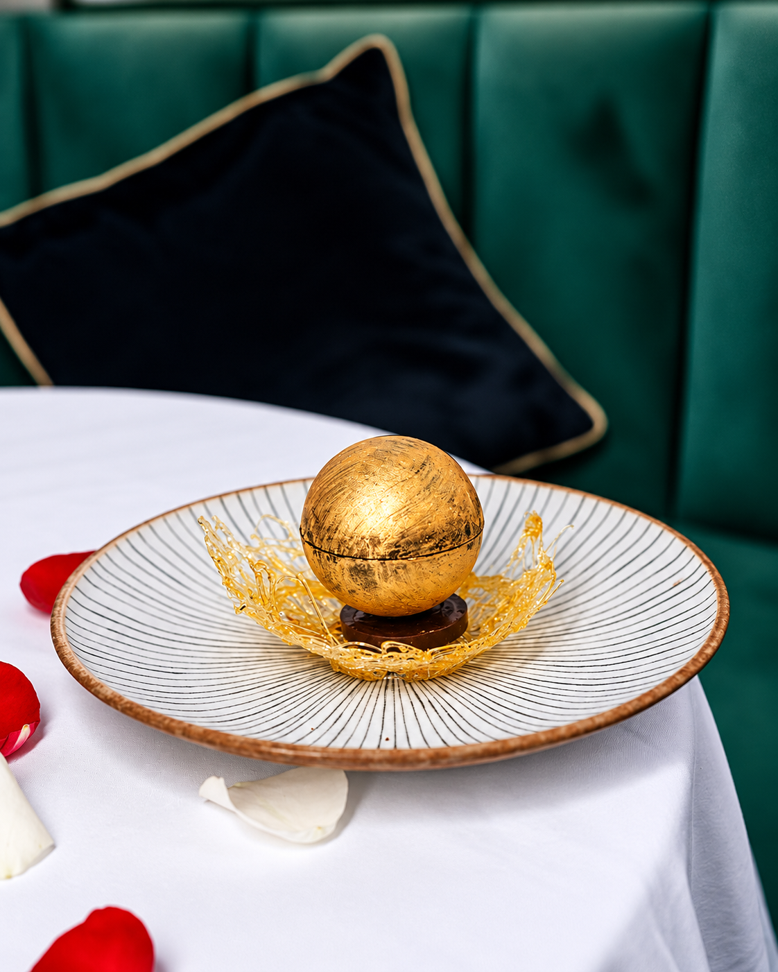 Luxurious dessert with golden sphere on artistic plate surrounded by rose petals at The Pods