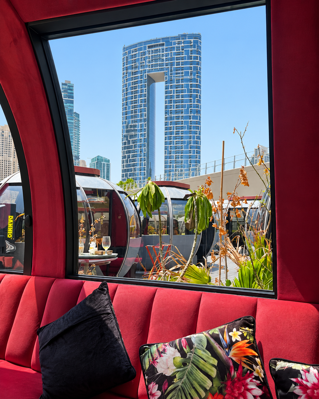 View from inside a red pod with a cityscape outside, featuring a modern skyscraper and other rounded outdoor pods.