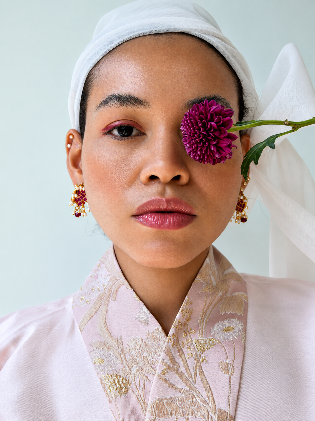 Rosi Ross Wearing Gold Elephant Earrings for Tiramisu Rosi Ross with a flower covering one eye, wearing elephant gold earrings from Tiramisu