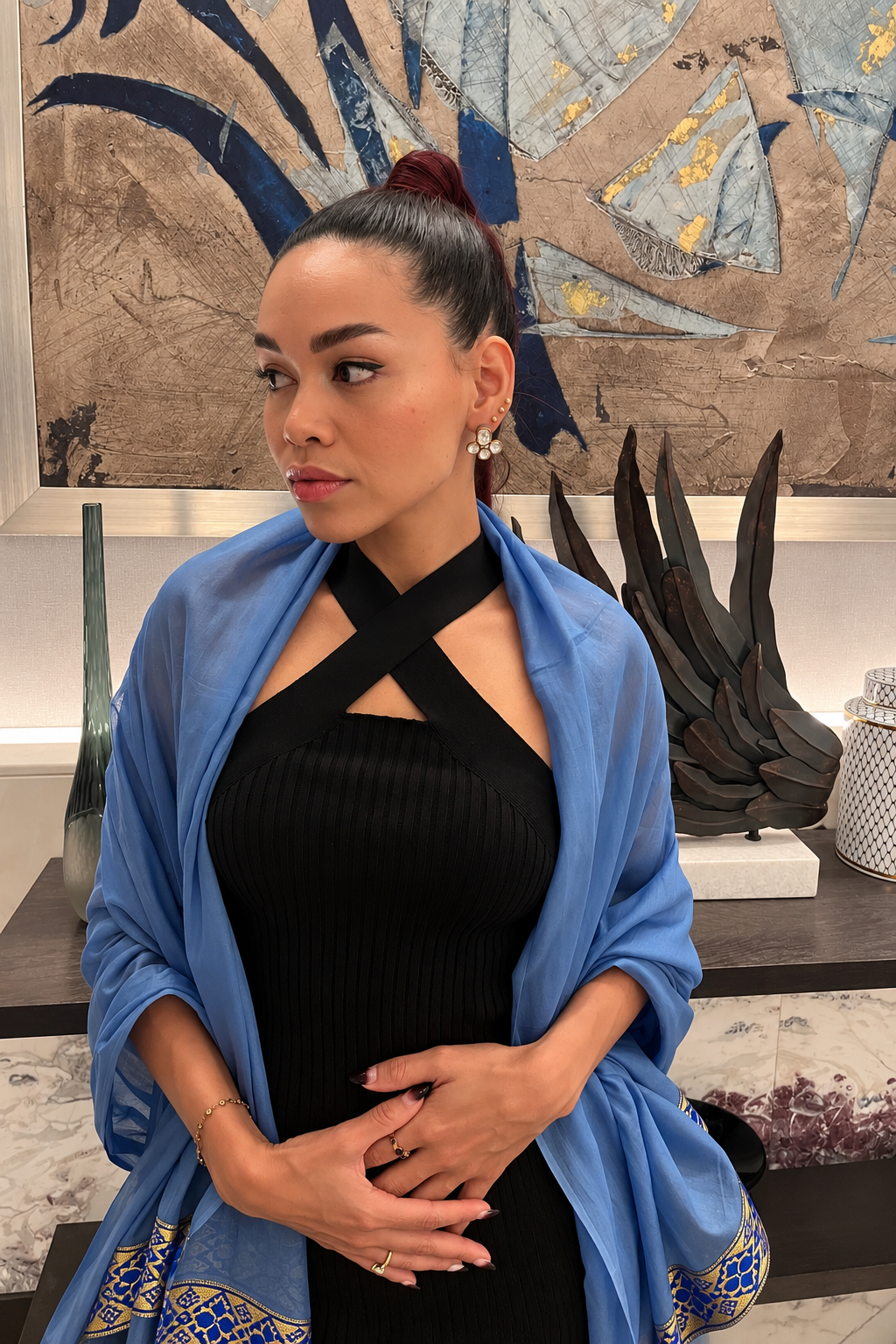 Elegant Tiramisu Styling with Blue Shawl Rosi Ross in a black dress with a blue shawl, wearing elegant earrings from Tiramisu and standing in front of abstract artwork.