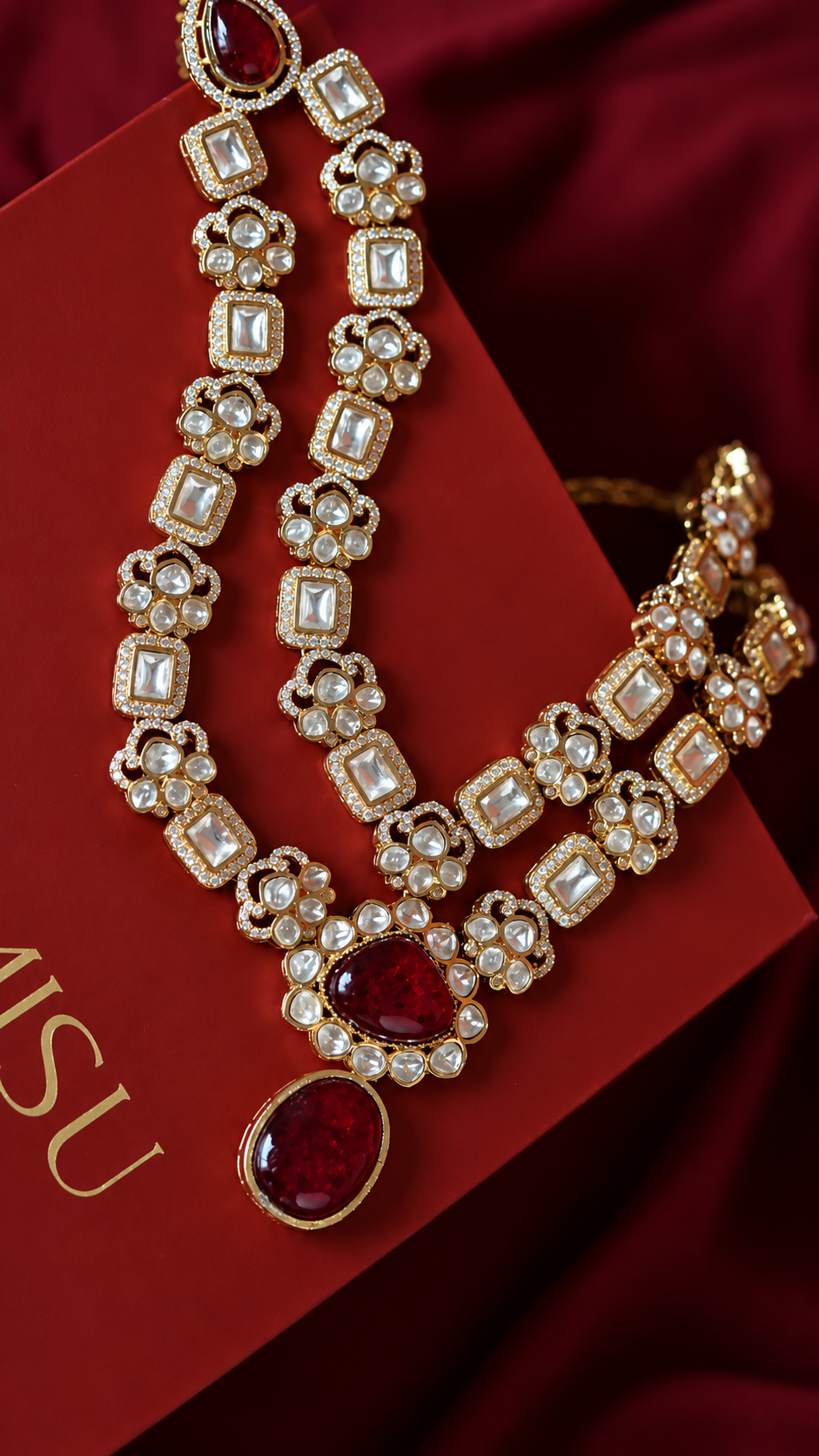 Elegant Gold Necklace with Red Stones from Tiramisu Gold jewelry set with red gemstones on a red background from Tiramisu