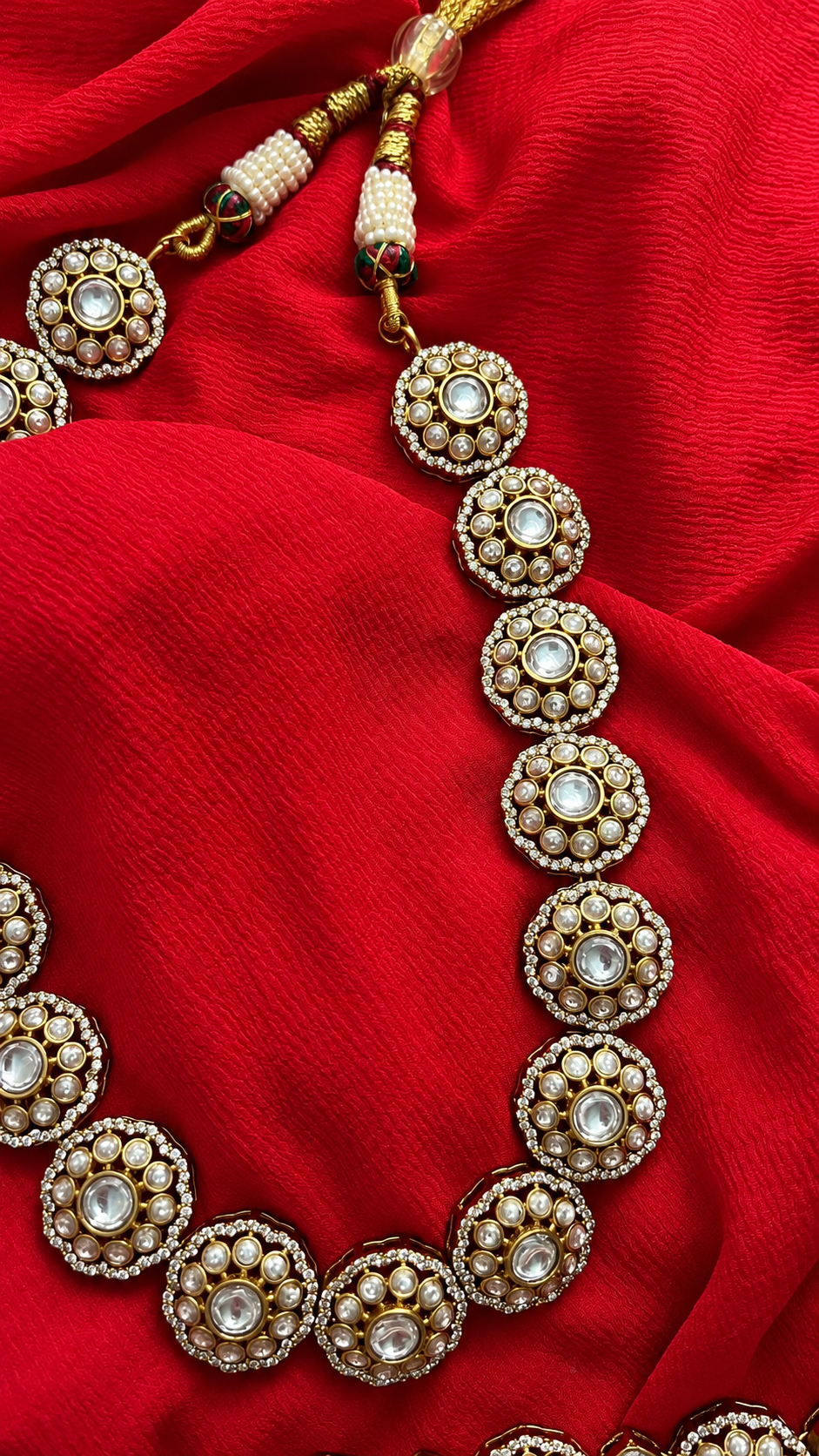 Gold and Pearl Necklace on Red Fabric from Tiramisu Intricate golden necklace with circular designs on red fabric from Tiramisu