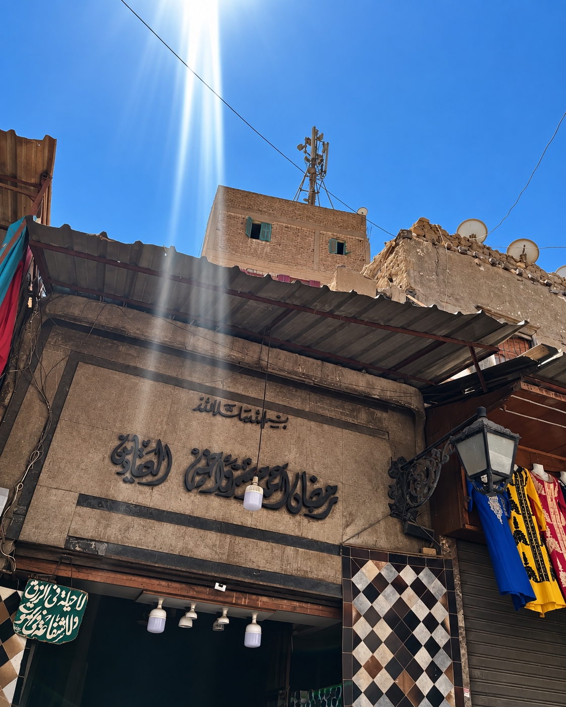 Arabic Storefront Under Blue Sky at Al Khalili Entryway to a historic market in Cairo with traditional Arabic signage and clothing displayed.