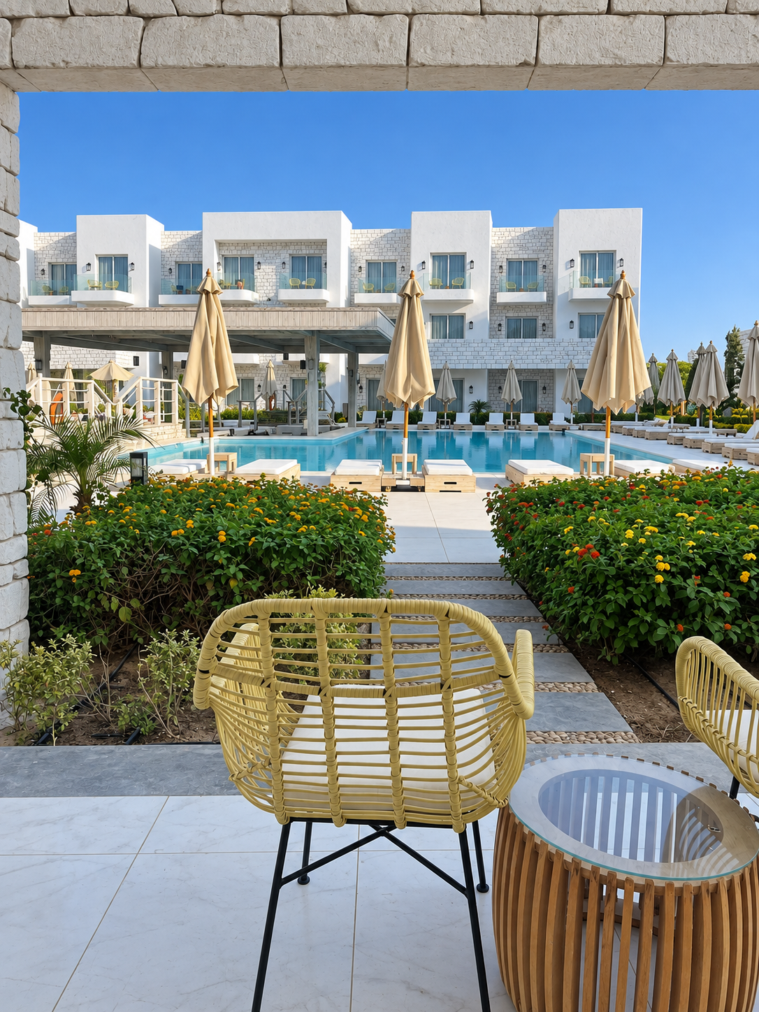 Resort Pool Area with Rattan Chairs at Tanoak Resort in Ain Sokhna Luxurious resort swimming pool with modern white buildings, lounge chairs, umbrellas, and lush green landscaping under a clear blue sky.