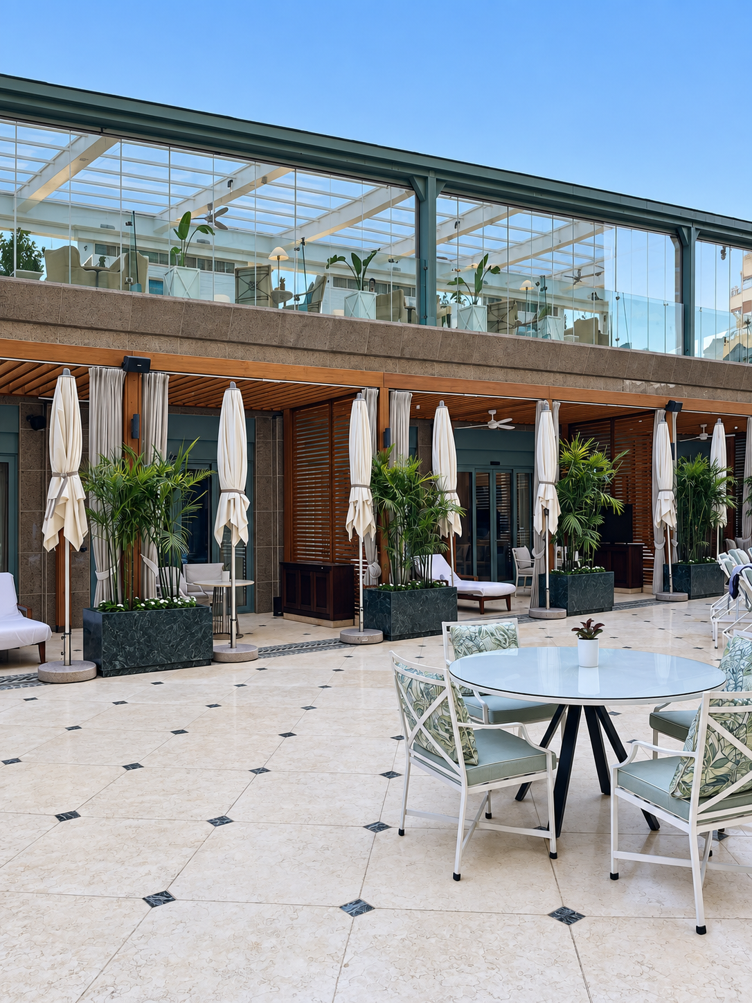 Outdoor patio with tables, chairs, and parasols near a modern building with glass walls at the Four Seasons Cairo