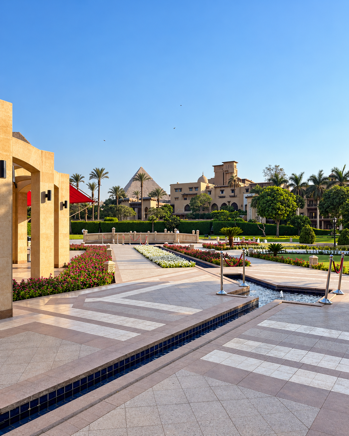 Landscape view of a tranquil garden with clear blue sky, palm trees, and distant view of pyramids and buildings at Marriott Mena House Hotel