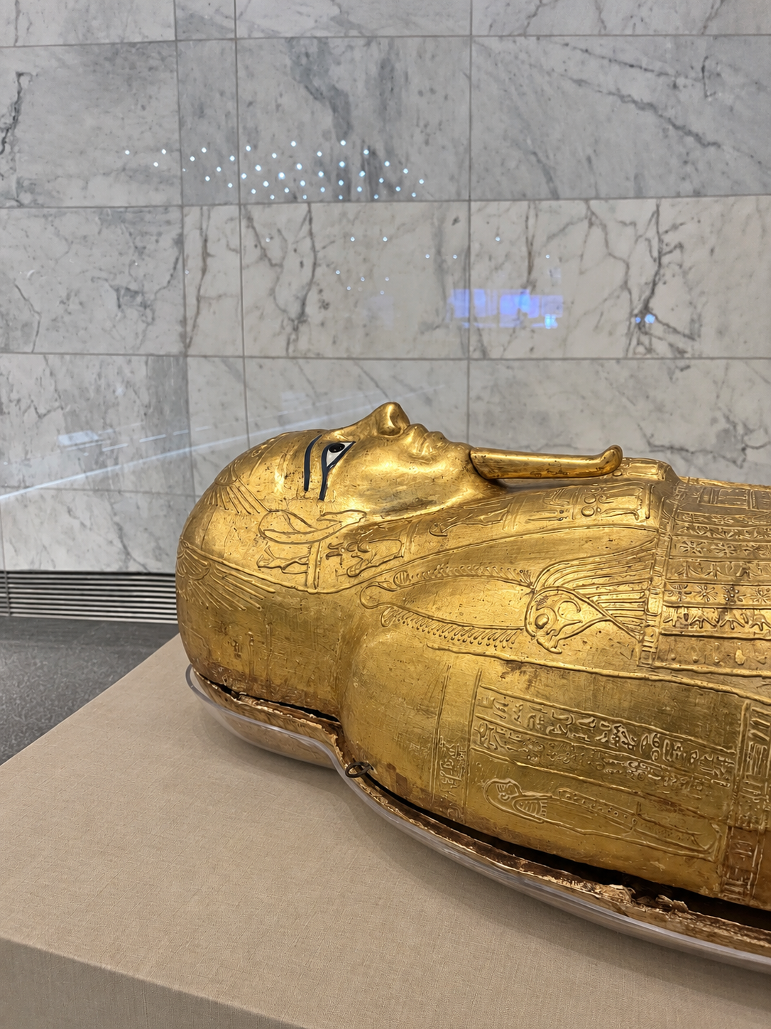 Sarcophagus Display at the National Museum of Egyptian Civilization's Gold mummy on display at the Egyptian Civilization Museum, placed on a beige surface with a marble wall background.