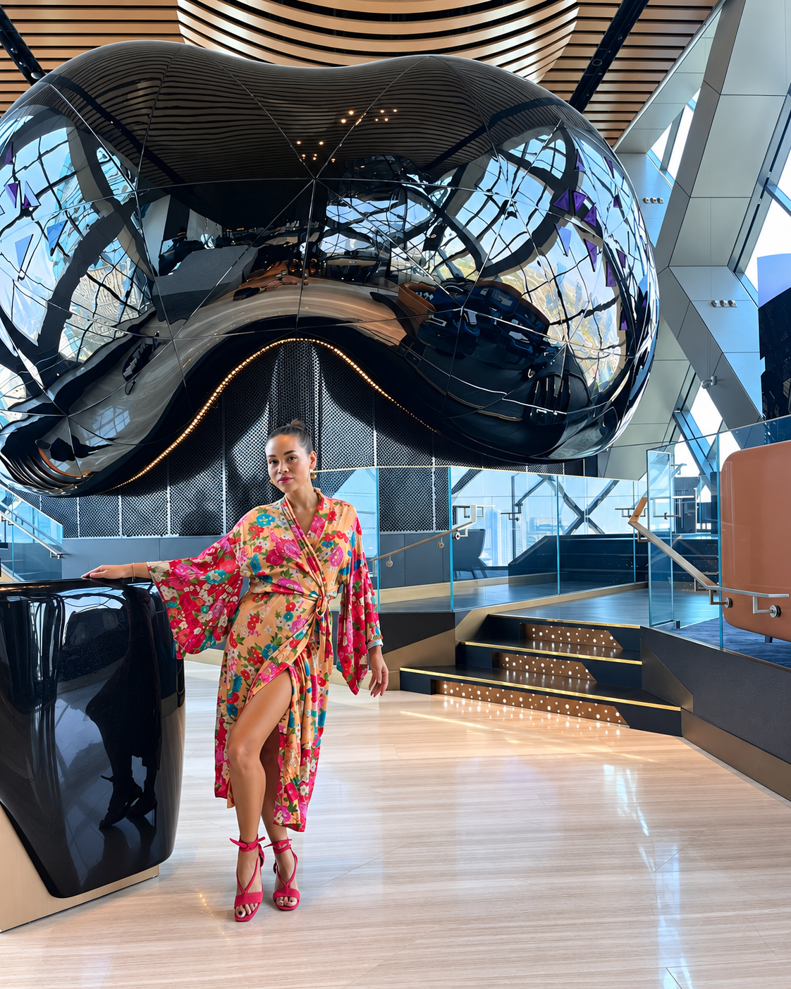 Rosi Ross in colorful floral dress standing in a modern interior with mirrored sculpture.