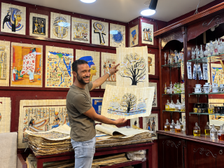 Mohammad holding papyrus painting in an art shop with various Egyptian-themed artworks displayed.