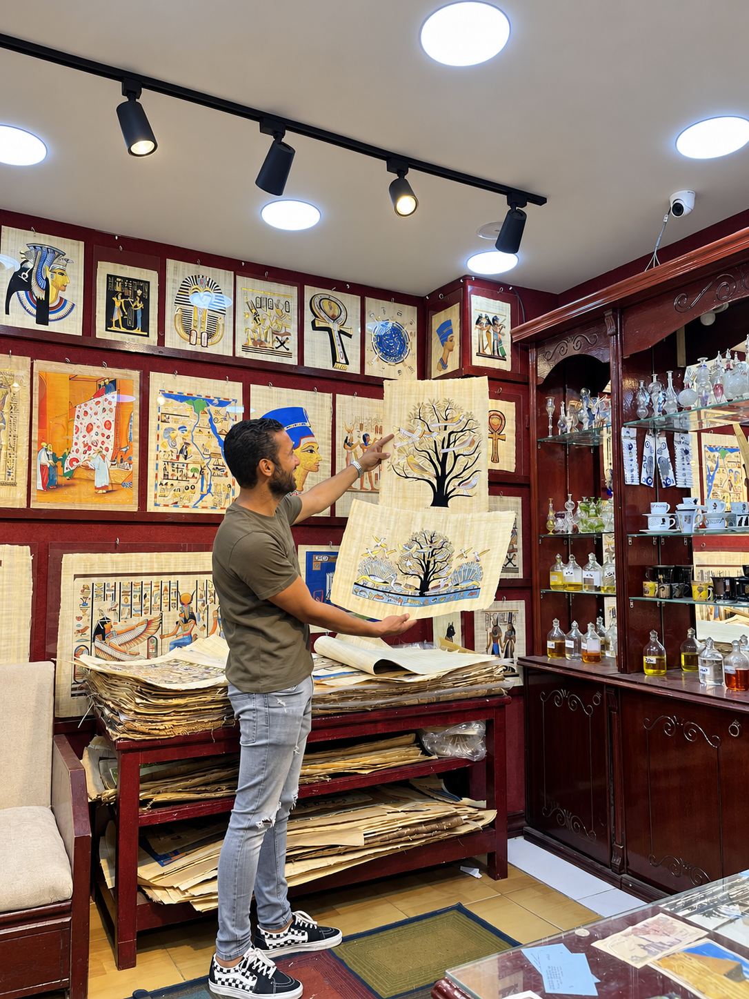 Mohammas in store holding a papyrus painting of a tree, surrounded by ancient Egyptian artwork.