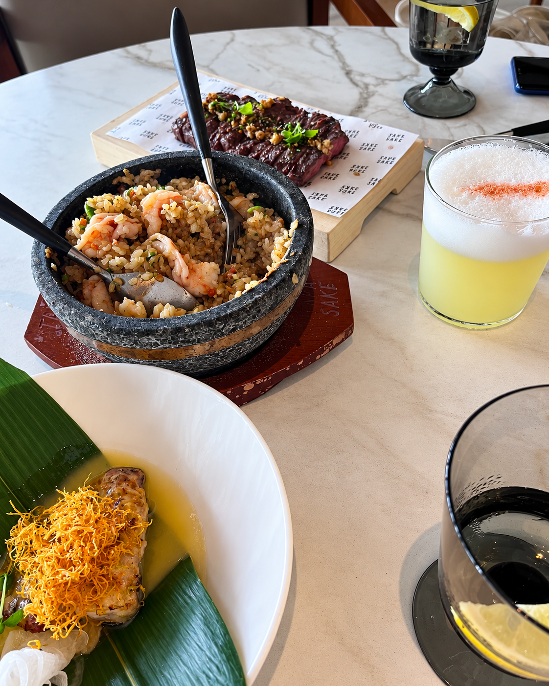 Gourmet Tapasake dishes with steak, fried rice, and a cocktail on a marble table.