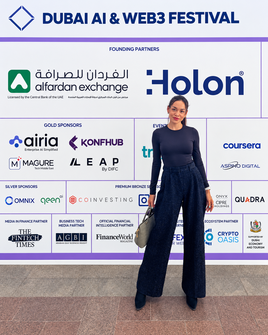 Rosi Ross at the Dubai AI and Web3 Festival Event Rosi Ross in navy blazer and wide-leg jeans poses in front of Dubai AI & Web3 Festival sponsor backdrop