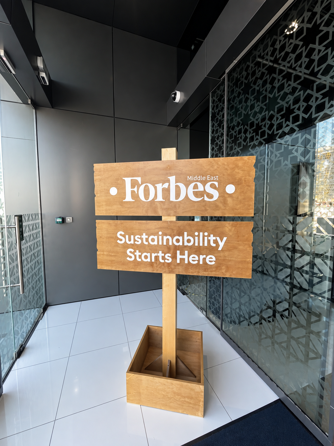RosiRoss Forbes Sustainability Summit AD Sign Forbes Middle East sign with "Sustainability Starts Here" in a modern office lobby with glass walls and white tiled floor.