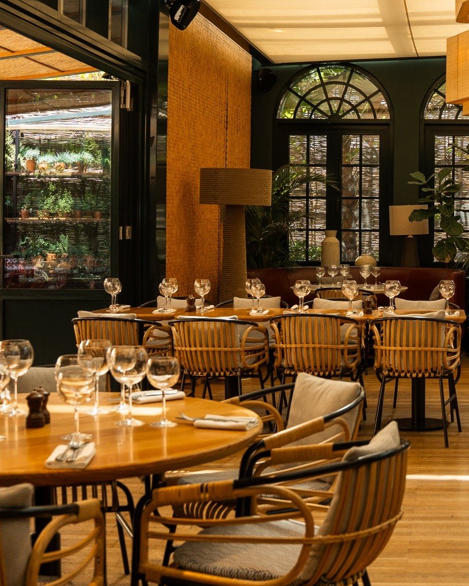 Eugene Eugene elegant modern restaurant dining room with wooden tables, striped rattan chairs, and lush green views through glass doors