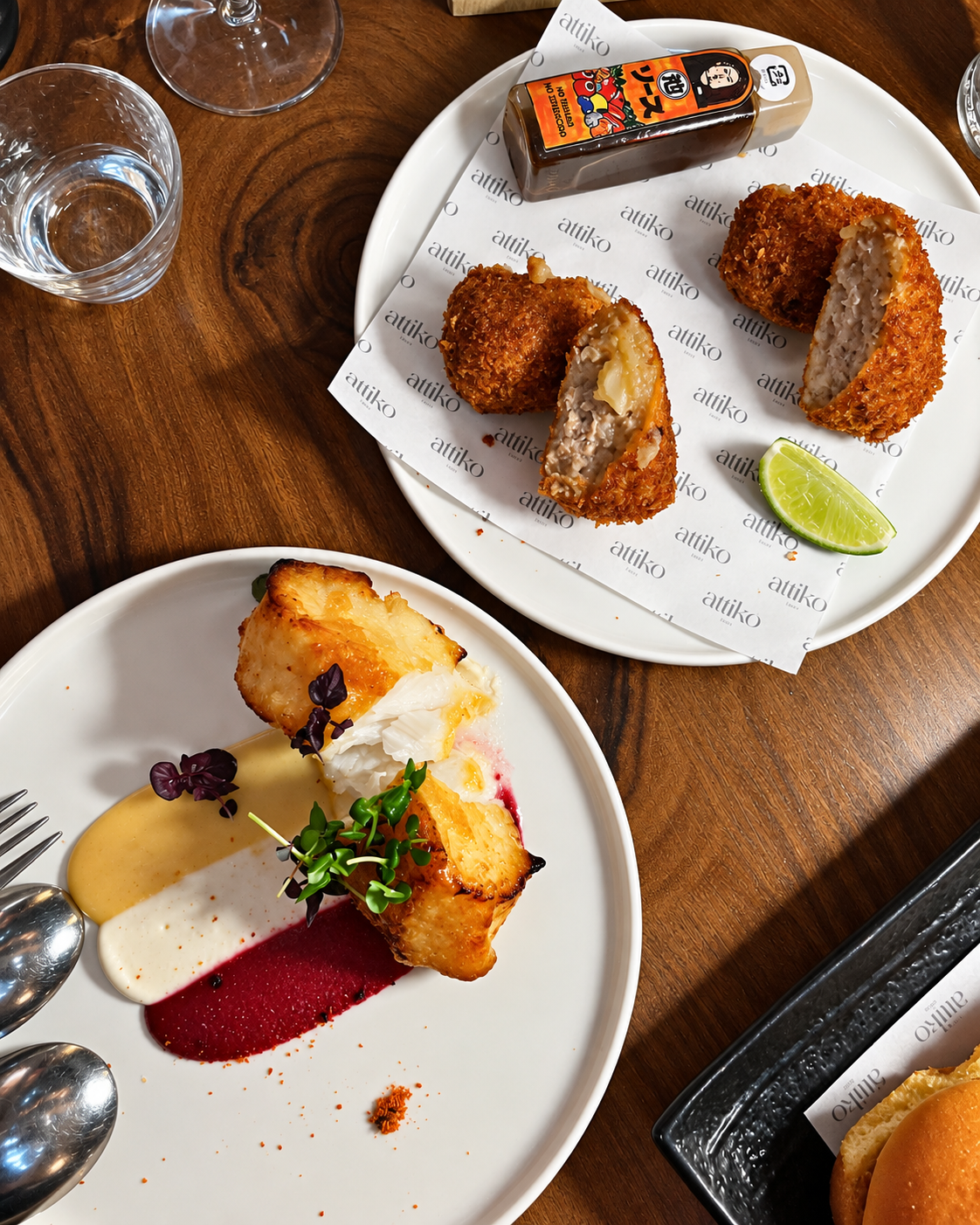 Fine Dining Appetizers and Plated Dishes at ATTIKO Dubai Plated fine dining appetizers with golden fried croquettes, seared scallop, and red sauce garnish on white plates at restaurant at ATTIKO Dubai