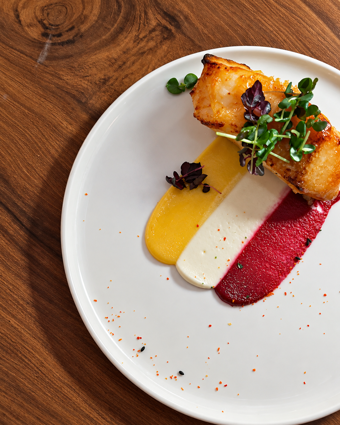 Artfully Plated Fine Dining Dish at Attiko Dubai Pan-seared fish on a white plate with yellow, white, and red purees, garnished with microgreens at Attiko Dubai