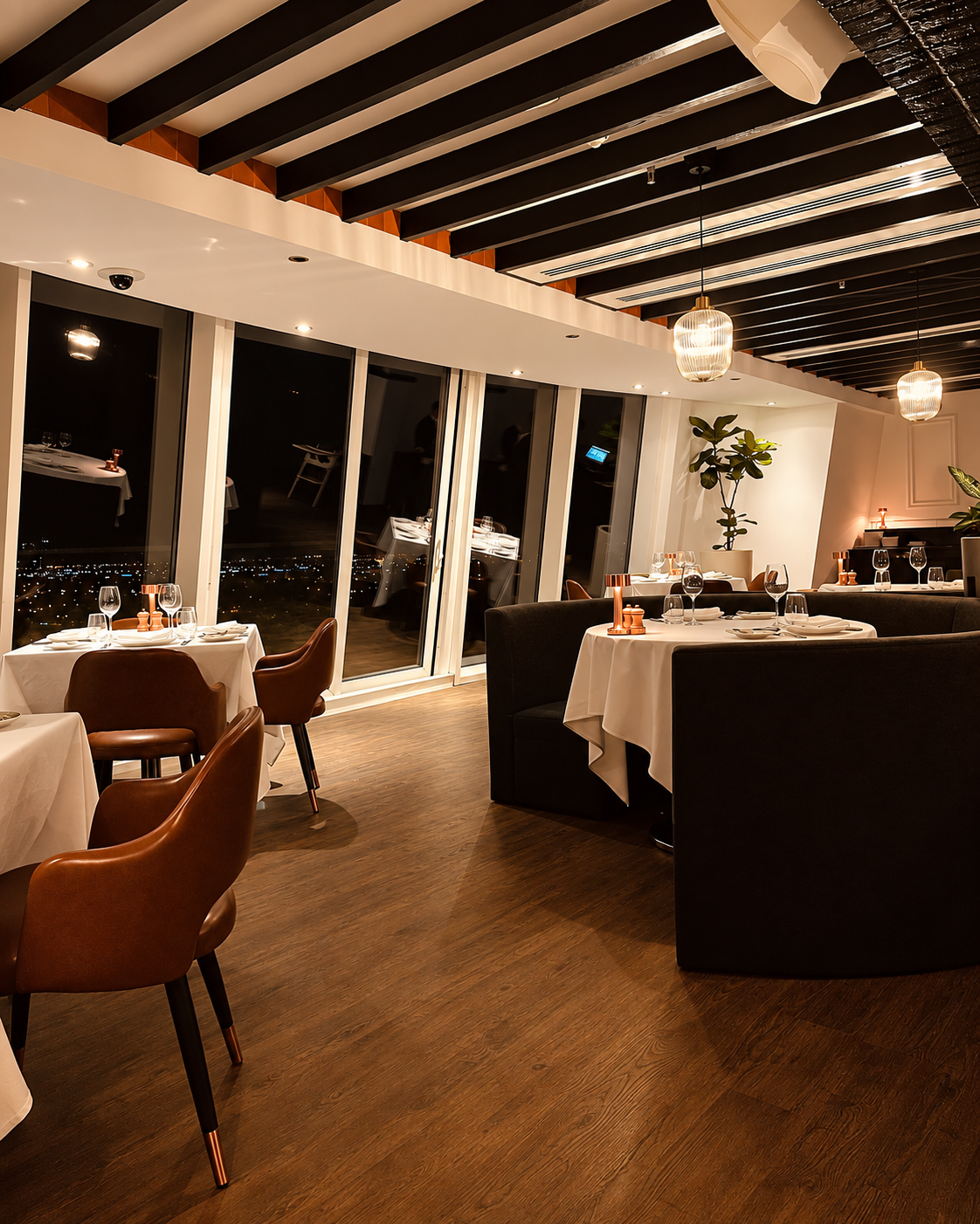 Bastion Dubai Modern Fine Dining Restaurant Interior Bastion Dubai modern fine dining restaurant interior with floor-to-ceiling windows overlooking city lights, dark wood beams, pendant lighting, and elegantly set tables