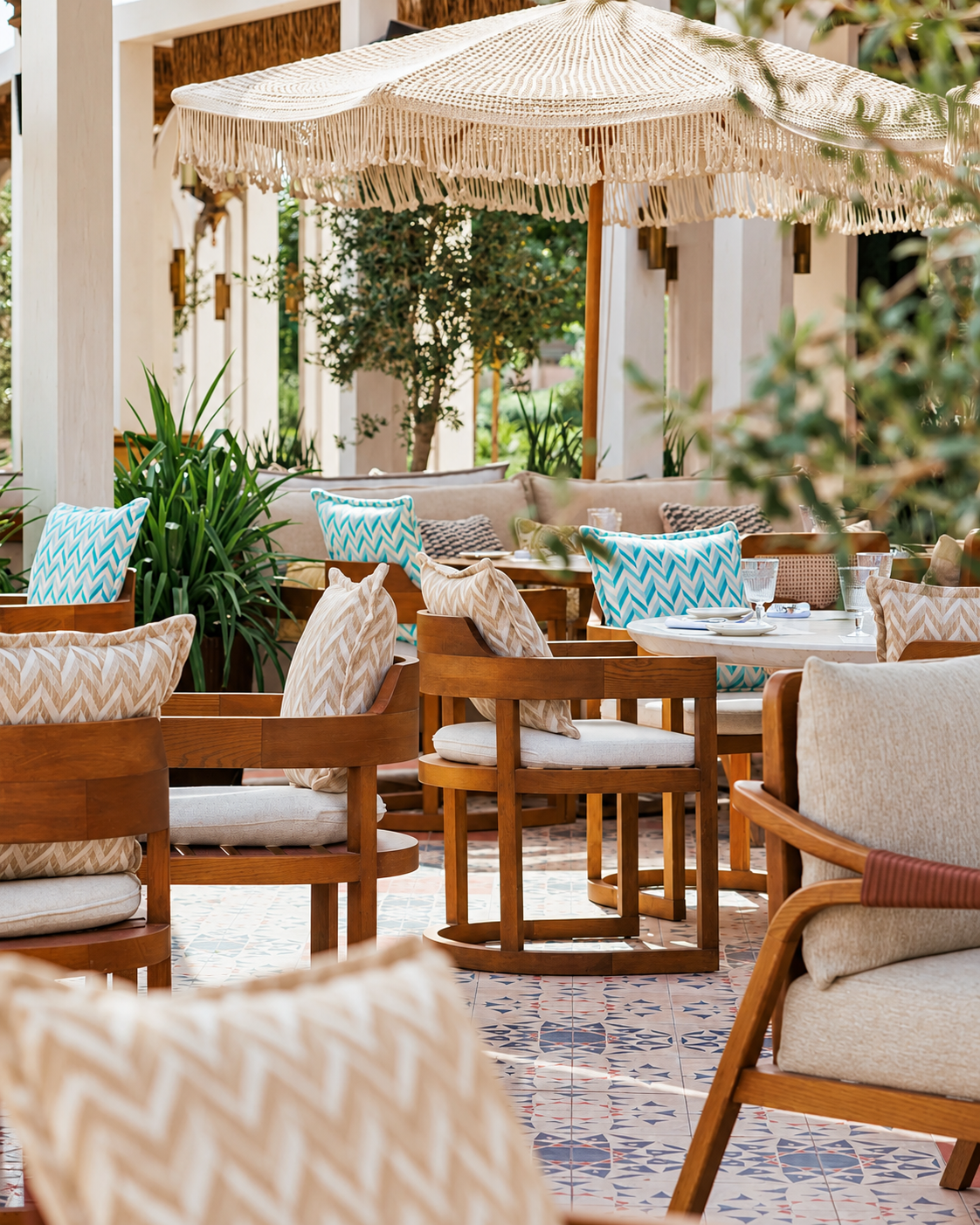 Nuska luxury outdoor patio seating area with wooden furniture, patterned cushions, and macram&eacute; fringe umbrella