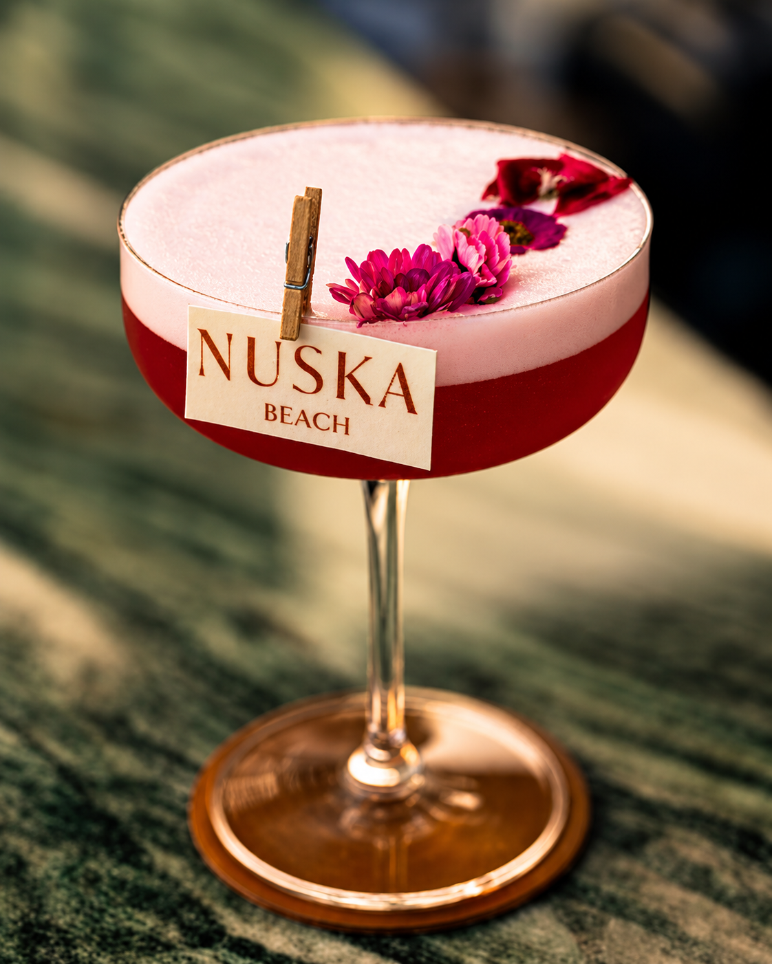 Nuska elegant red and cream cocktail in a coupe glass garnished with dried pink flowers and a cinnamon stick