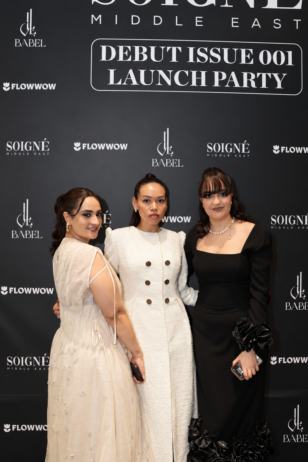 Soigné Middle East Debut Issue Launch Party Rosi Ross and Soigne Founders posing at a debut issue launch party for Soigné Middle East with branded backdrop
