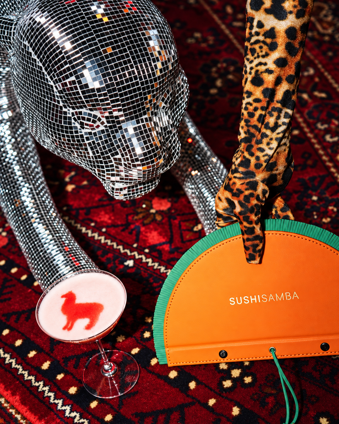 Glamorous disco night fashion statement at Sushi Samba Sushi Samba disco ball head with leopard print leg and orange Sushi Samba branded clutch against dark background