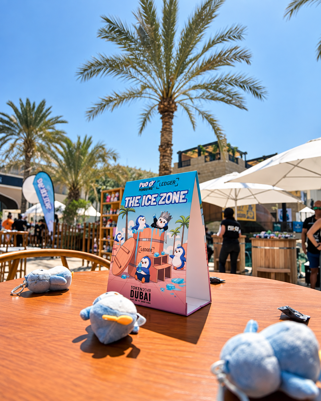 Branded ice zone promotional box on orange table with palm trees and market stalls in background Pudgy Penguins at Token 2049 Dubai Rosi Ross