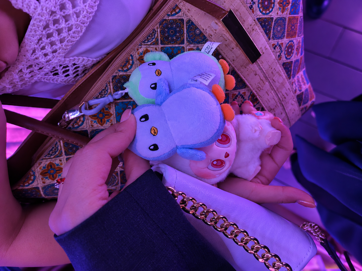 Close-up of three cute, colorful plush keychains with cartoon eyes, one blue and green, one pale pink, and one white.